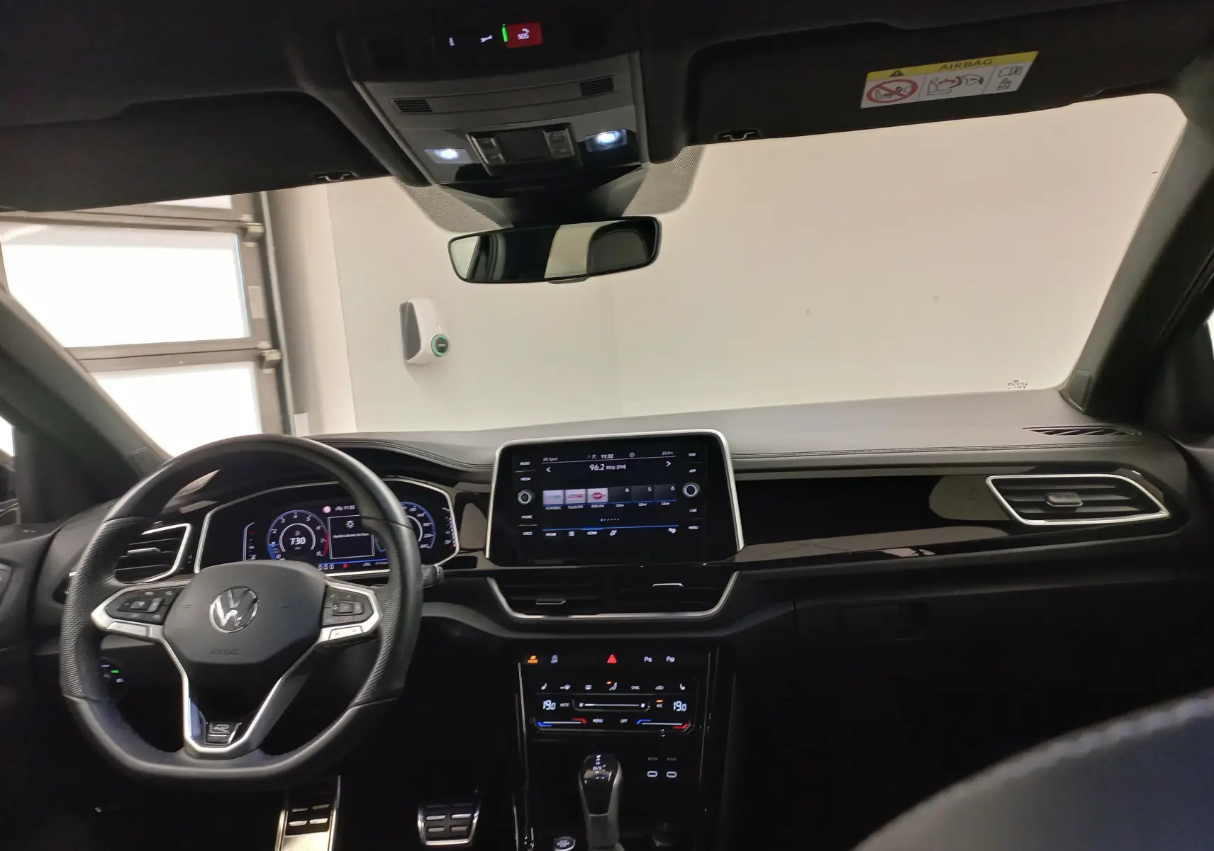 Vue intérieure avant du tableau de bord noir du Volkswagen T-Roc 2025 avec écran tactile central et volant multifonction.