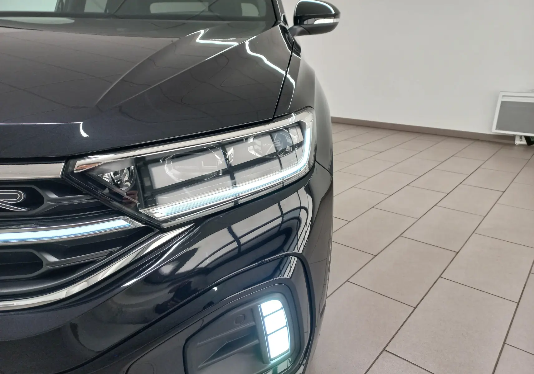 Gros plan sur l'avant droit du Volkswagen T-Roc 2025 noir intense nacré avec projecteurs Matrix LED allumés.