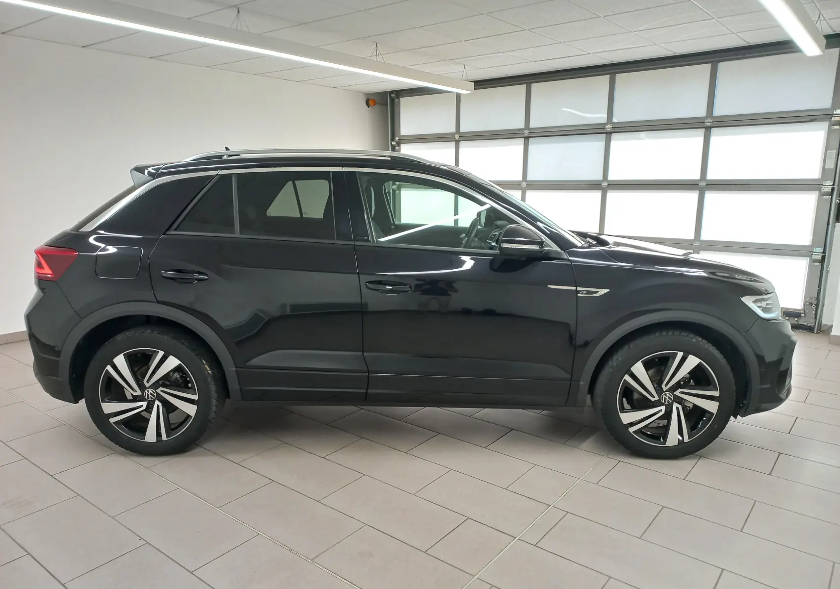 Vue de profil côté gauche du Volkswagen T-Roc 1.5 TSI 150 DSG7 R-Line en noir intense nacré, avec jantes distinctives et lignes dynamiques.