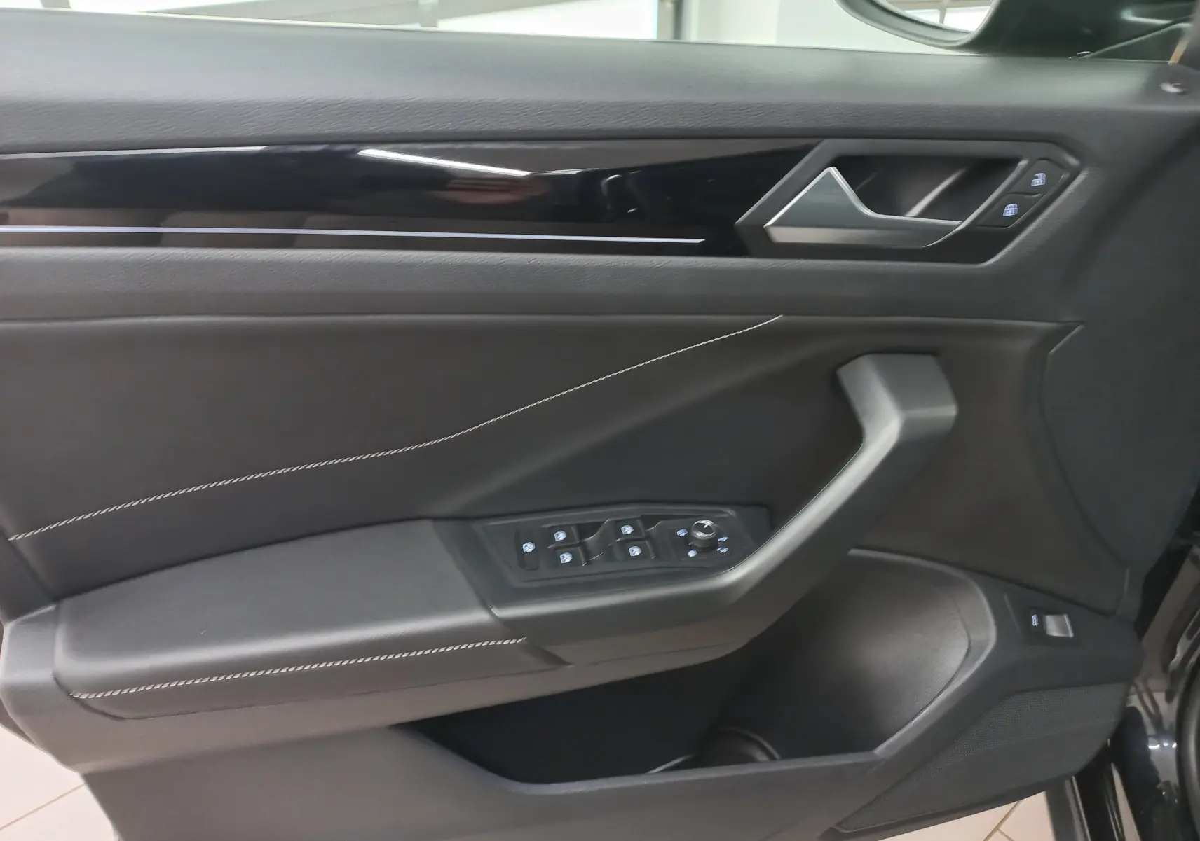 Gros plan sur la porte avant gauche noire du Volkswagen T-Roc 2025 avec commandes de vitres et surpiqûres blanches.