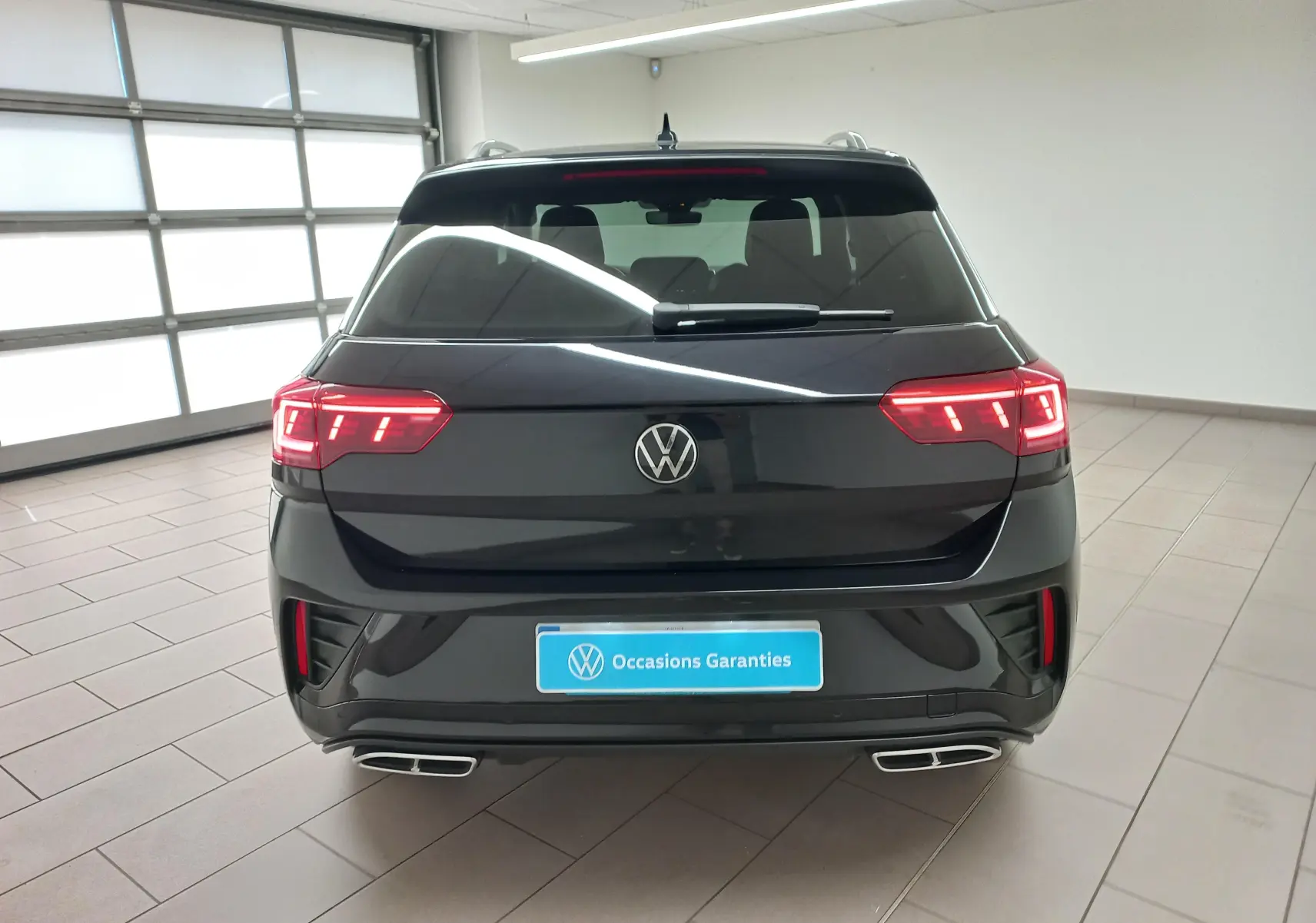 Vue arrière d'un Volkswagen T-Roc 1.5 TSI 150 DSG7 R-Line noir intense nacré avec feux LED allumés en intérieur.