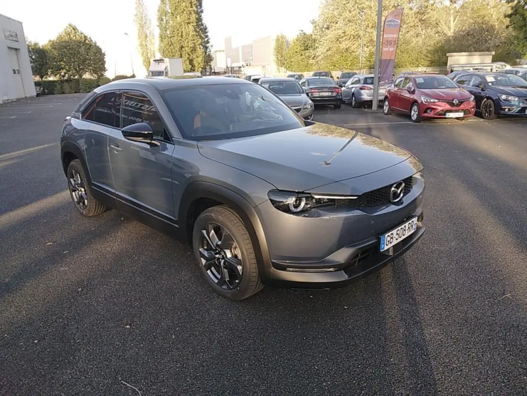 Vue 3/4 avant d'une Mazda MX-30 gris électrique, avec ses phares ronds caractéristiques et ses jantes noires distinctives.