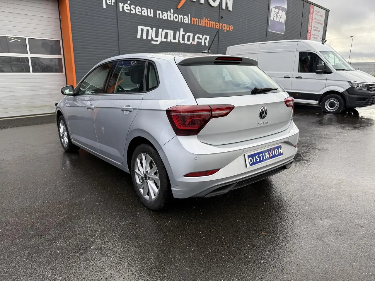 Volkswagen Polo 2025 argent métallisé vue 3/4 arrière droit sur sol mouillé devant un garage.