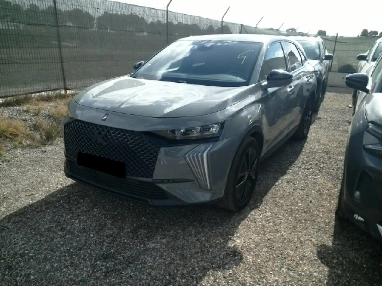 DS7 1.6 E-Tense gris laqué en 3/4 avant droit, avec calandre noire et feux LED distinctifs en forme de griffes.