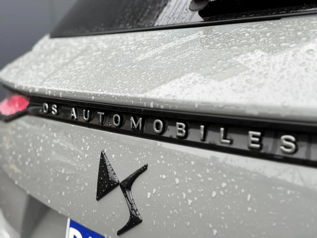 Gros plan sur l'arrière gris laqué du DS7 2024 avec logo DS et lettrage DS Automobiles sous la pluie.