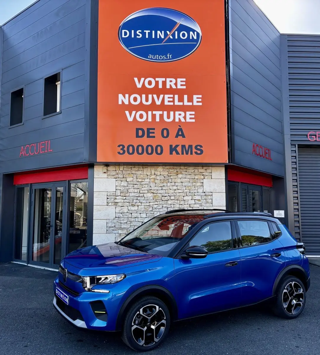 Citroën C3 100 BVM PLUS bleu vue 3/4 avant avec toit noir et jantes distinctives, devant un bâtiment commercial.