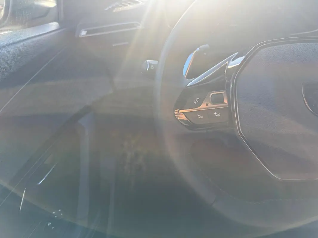 Vue partielle de l’intérieur du Peugeot 2008 Hybrid gris, avec le volant multifonction et commandes au volant visibles.
