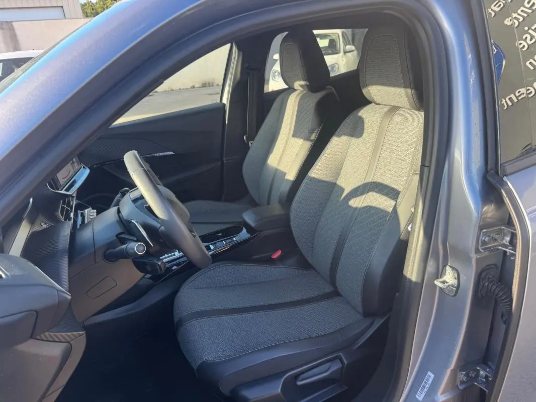 Intérieur avant droit du Peugeot 2008 Hybrid gris 2024, sièges tissu gris avec console centrale et volant visible.