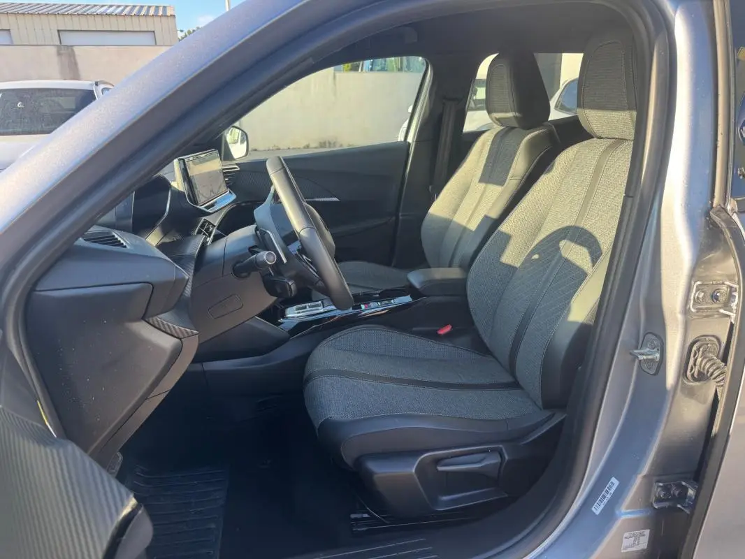 Intérieur avant droit du Peugeot 2008 Hybrid gris 2024, sièges tissu, tableau de bord avec écran tactile et volant.