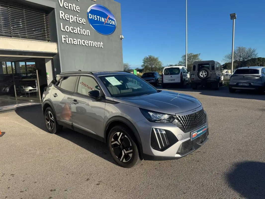 Peugeot 2008 Hybrid gris en 3/4 avant droit, avec barres de toit et jantes alliage 17 pouces, stationnée devant un concessionnaire.