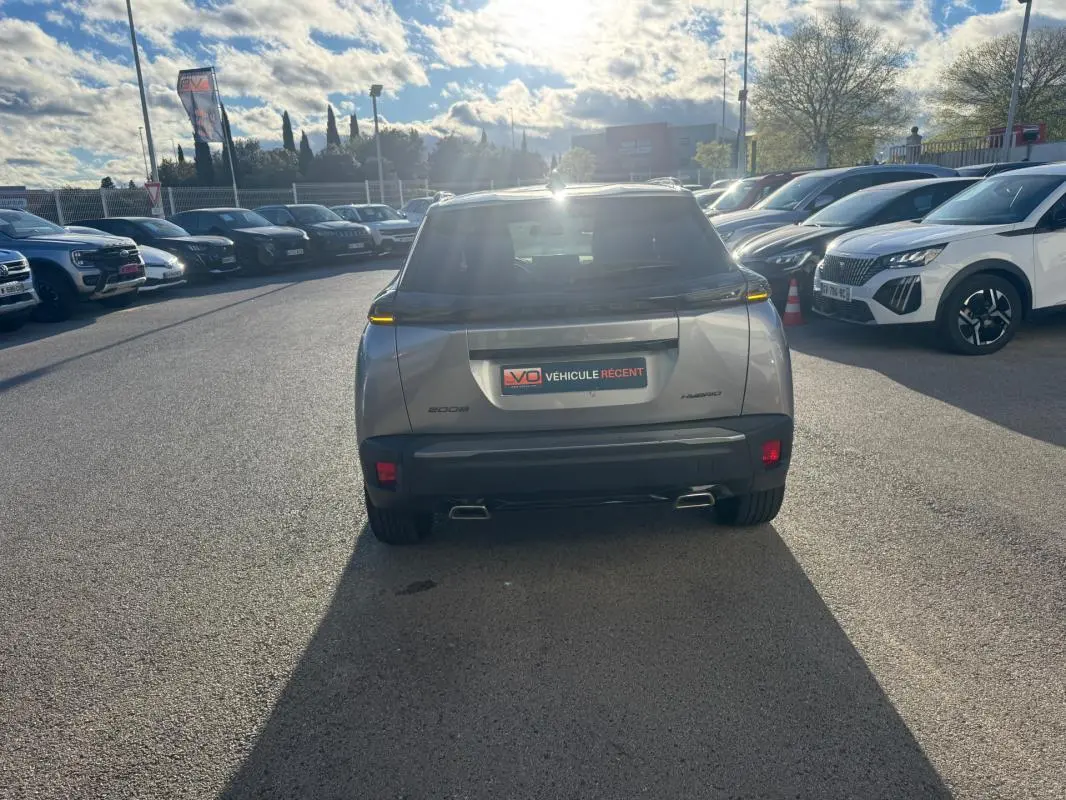 Vue arrière d’un Peugeot 2008 Hybrid gris 2024 avec feux LED fins et double sortie d’échappement visible en concession.