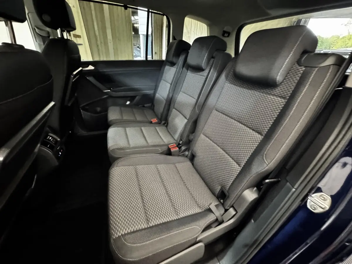 Vue intérieure côté droit sur la deuxième rangée de sièges gris du Volkswagen Touran bleu 2024, version 7 places.