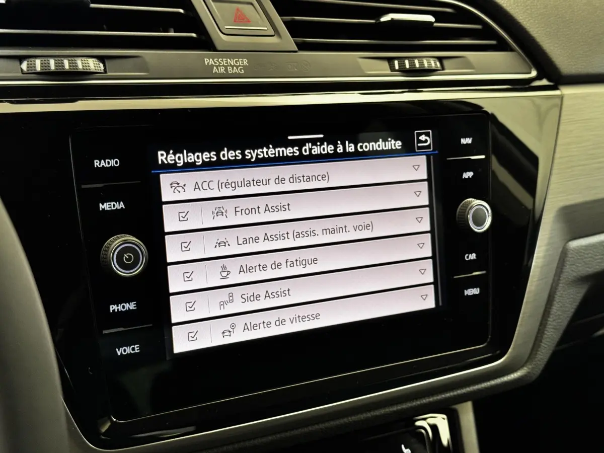 Écran tactile central du Volkswagen Touran 2024 affichant les réglages des aides à la conduite, intérieur noir.