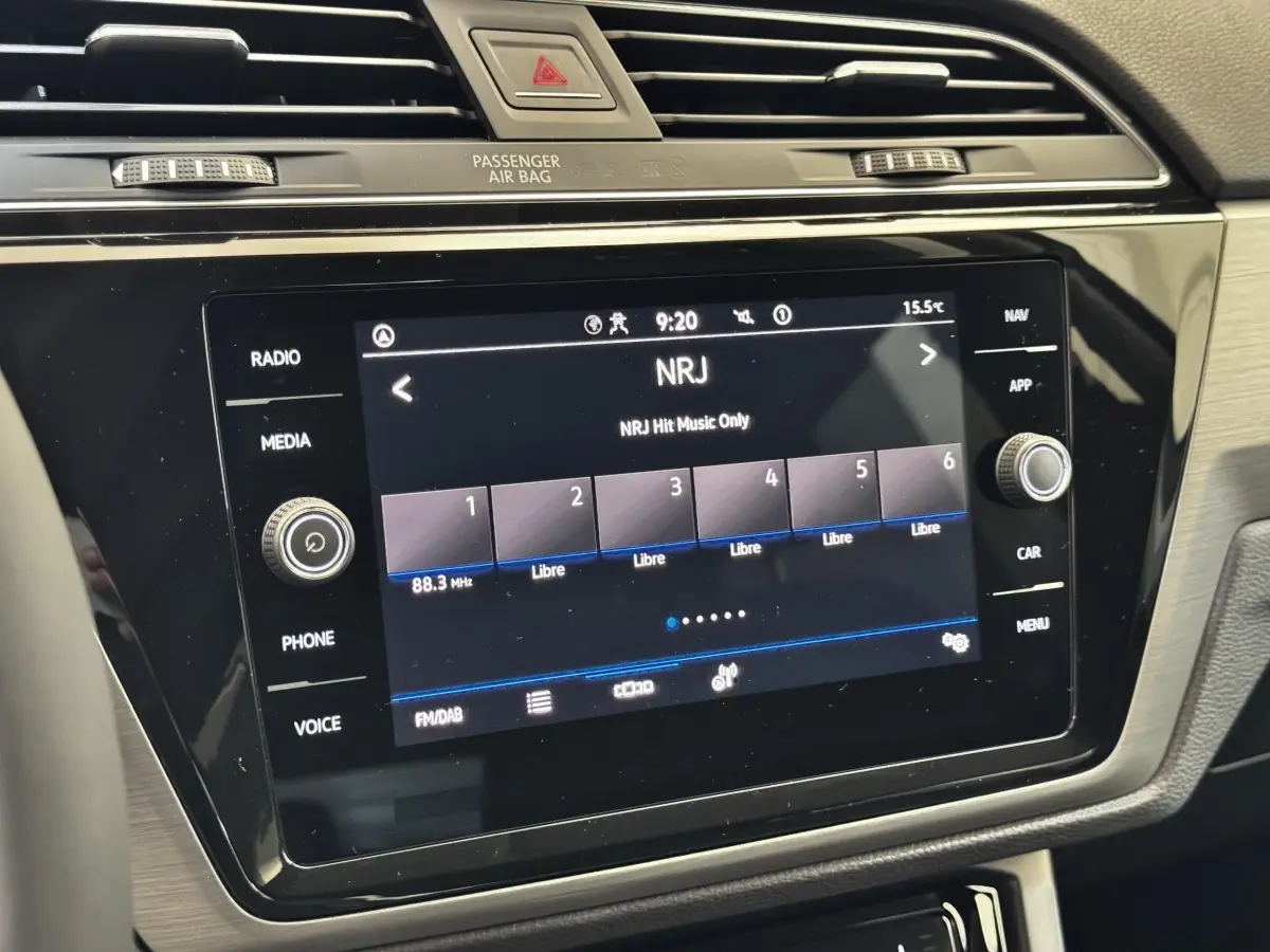 Gros plan sur l’écran tactile central noir du tableau de bord du Volkswagen Touran 2024 affichant la radio NRJ.