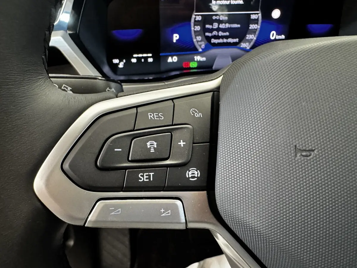Gros plan sur le volant multifonctions du Volkswagen Touran 2024, boutons de régulateur de vitesse visibles, intérieur noir.