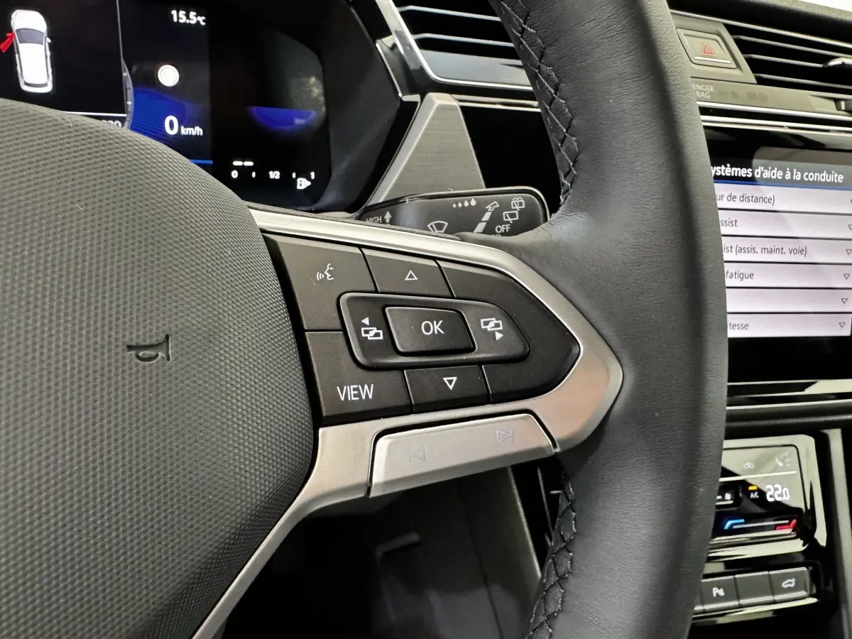 Gros plan sur le volant cuir noir côté gauche du Volkswagen Touran 2024 avec commandes multifonctions et tableau de bord digital.