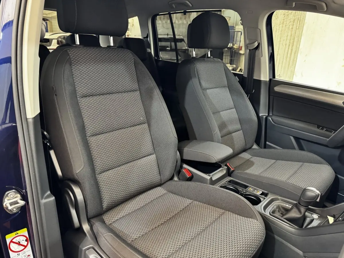 Vue intérieure côté avant droit du Volkswagen Touran 2024 bleu, sièges tissu gris avec console centrale et levier de vitesse.