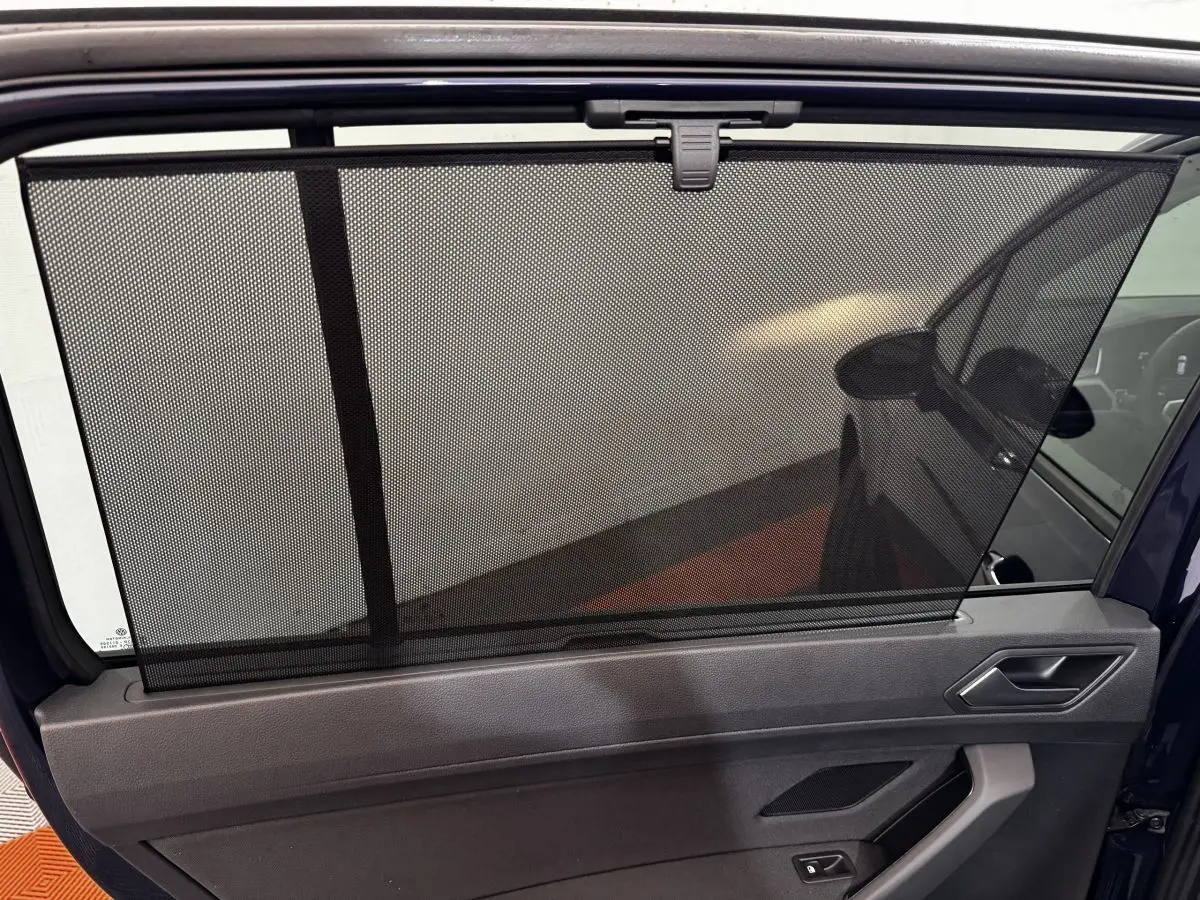 Vue intérieure de la porte arrière droite d’un Volkswagen Touran bleu 2024 avec pare-soleil en filet déployé.