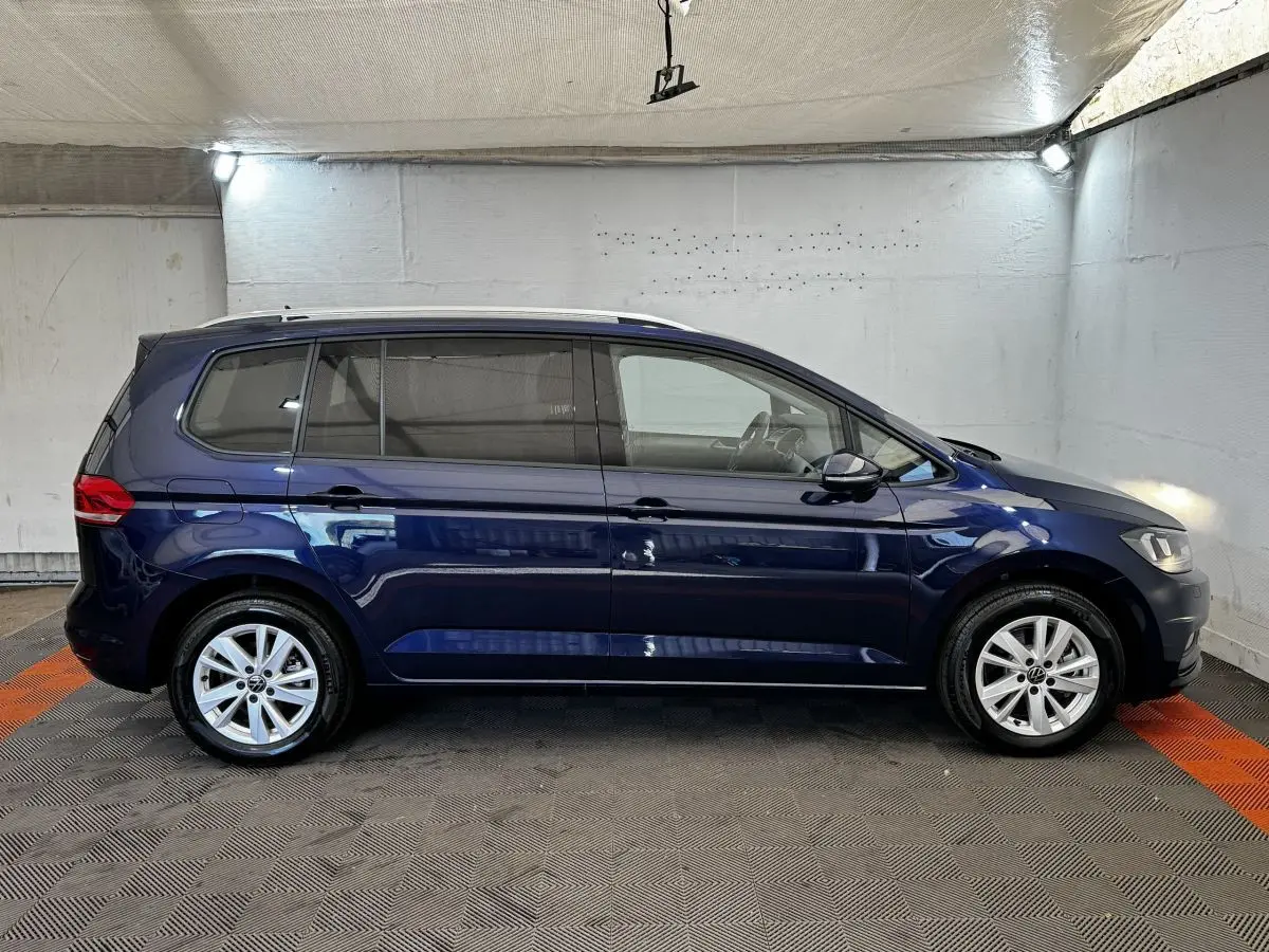 Vue latérale droite d'un Volkswagen Touran bleu 2024, montrant ses lignes épurées et ses jantes alliage.