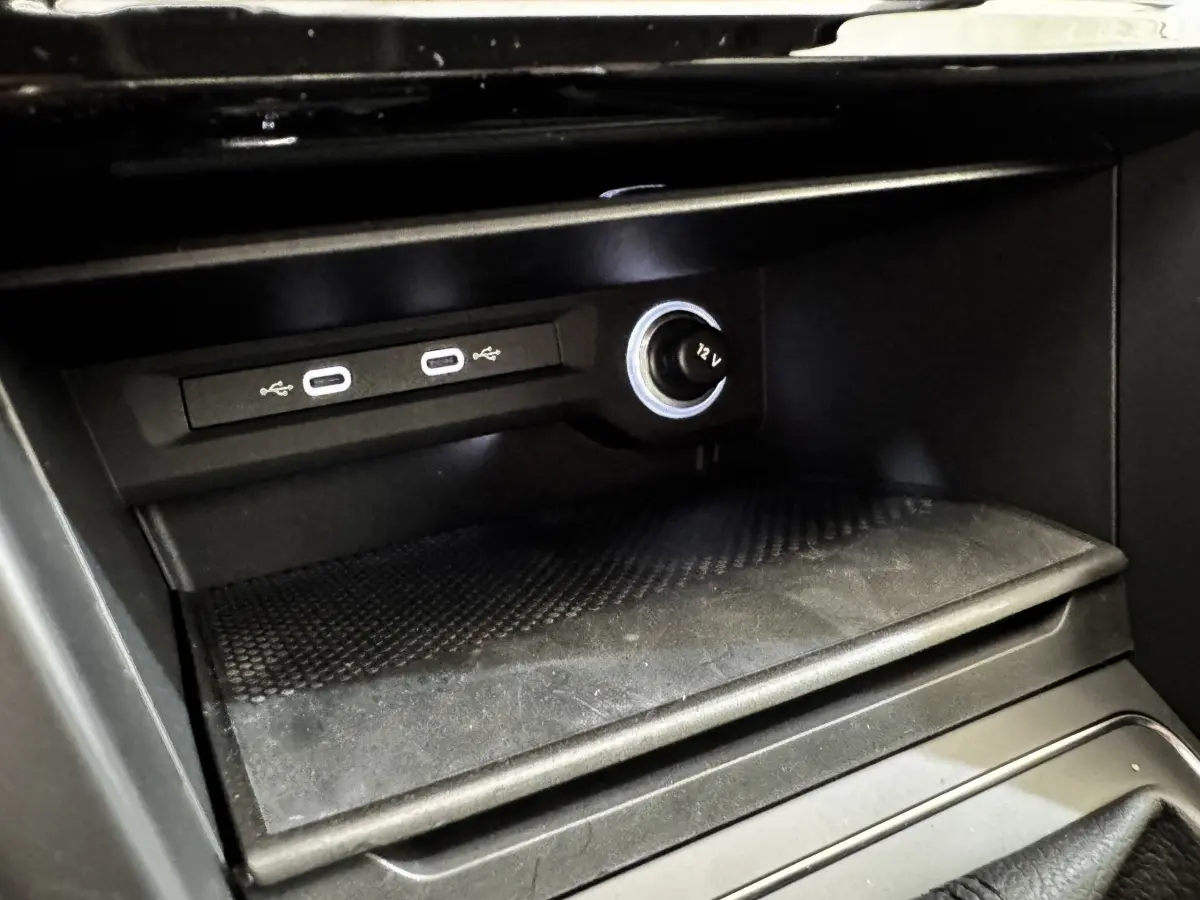 Gros plan sur la console centrale noire du Volkswagen Touran 2024, montrant prises USB et prise 12V éclairée.