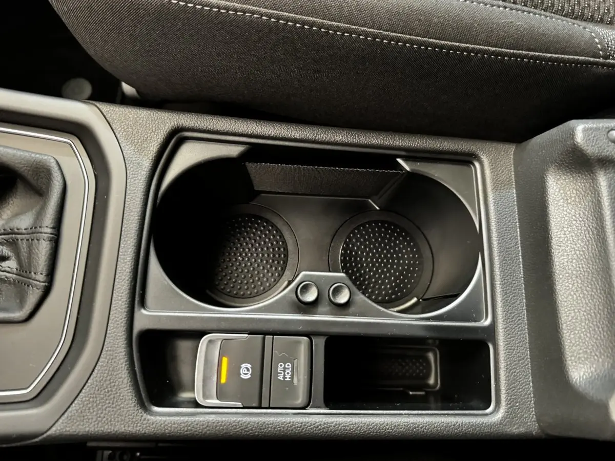 Gros plan sur la console centrale noire du Volkswagen Touran 2024, avec porte-gobelets et commandes frein à main électrique.