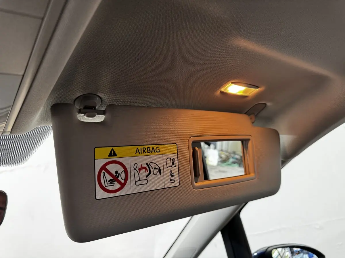 Vue intérieure du pare-soleil côté conducteur du Volkswagen Touran 2024 bleu avec miroir et avertissement airbag éclairé.