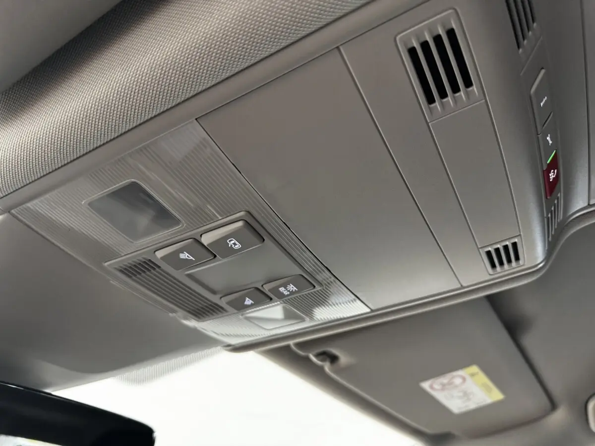 Vue en plongée sur le plafonnier gris avec commandes d’éclairage et ventilation du Volkswagen Touran 2024 bleu.