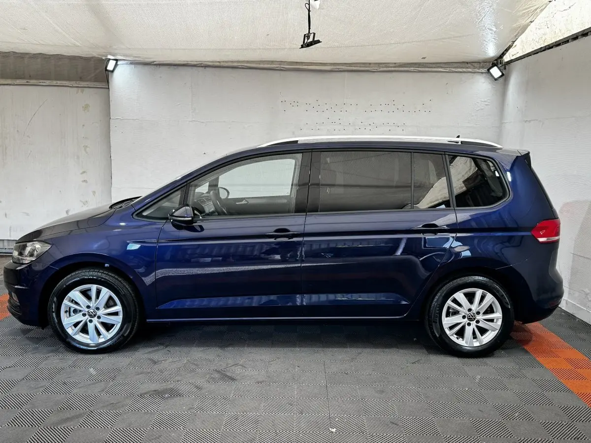 Profil latéral droit d'un Volkswagen Touran bleu 2024 avec jantes alliage et toit ouvrant visible en intérieur neutre.
