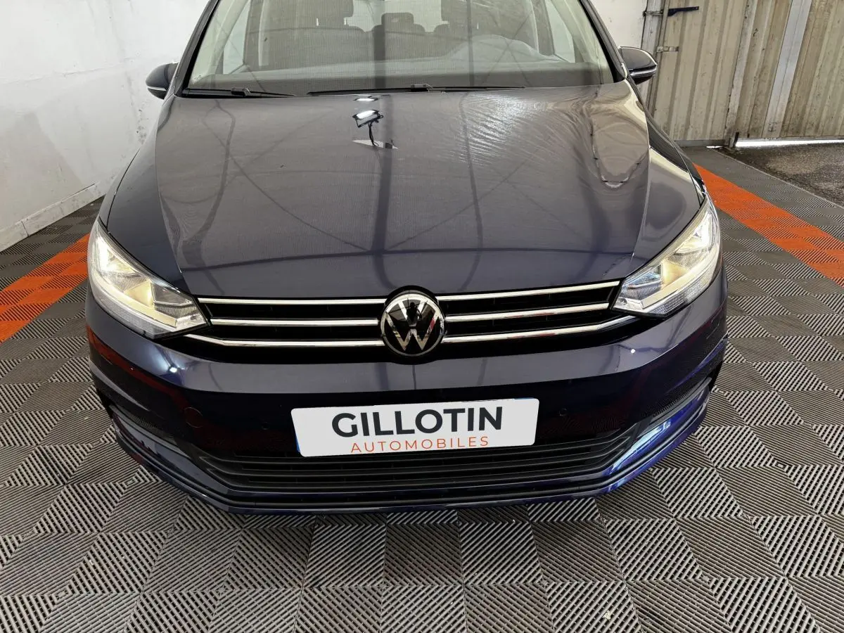 Vue avant rapprochée d’un Volkswagen Touran bleu 2024 avec calandre chromée et phares allumés.