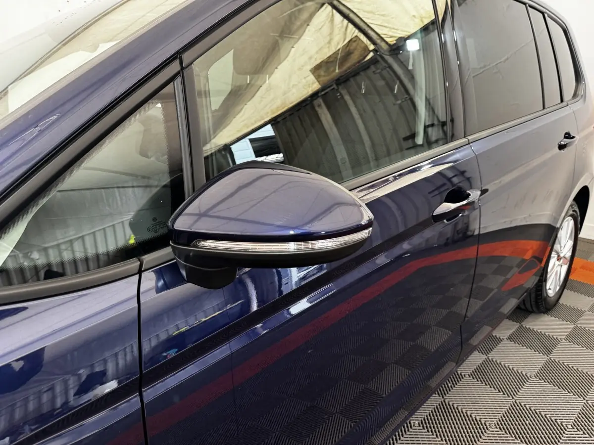 Vue rapprochée du côté gauche d’un Volkswagen Touran bleu 2024, mettant en valeur le rétroviseur avec clignotant intégré.