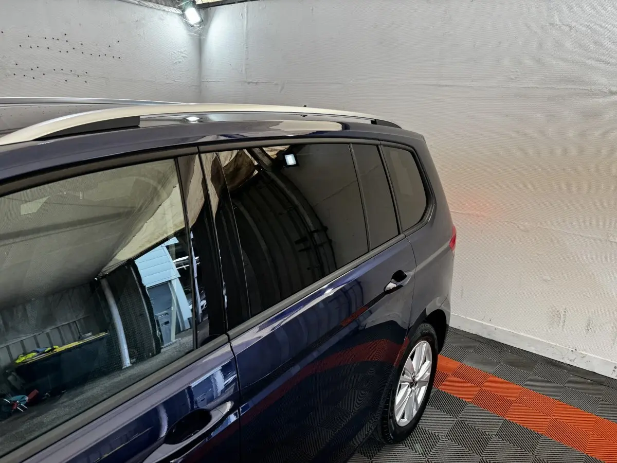 Vue latérale droite du Volkswagen Touran bleu 2024, mettant en valeur les vitres teintées et les barres de toit chromées.