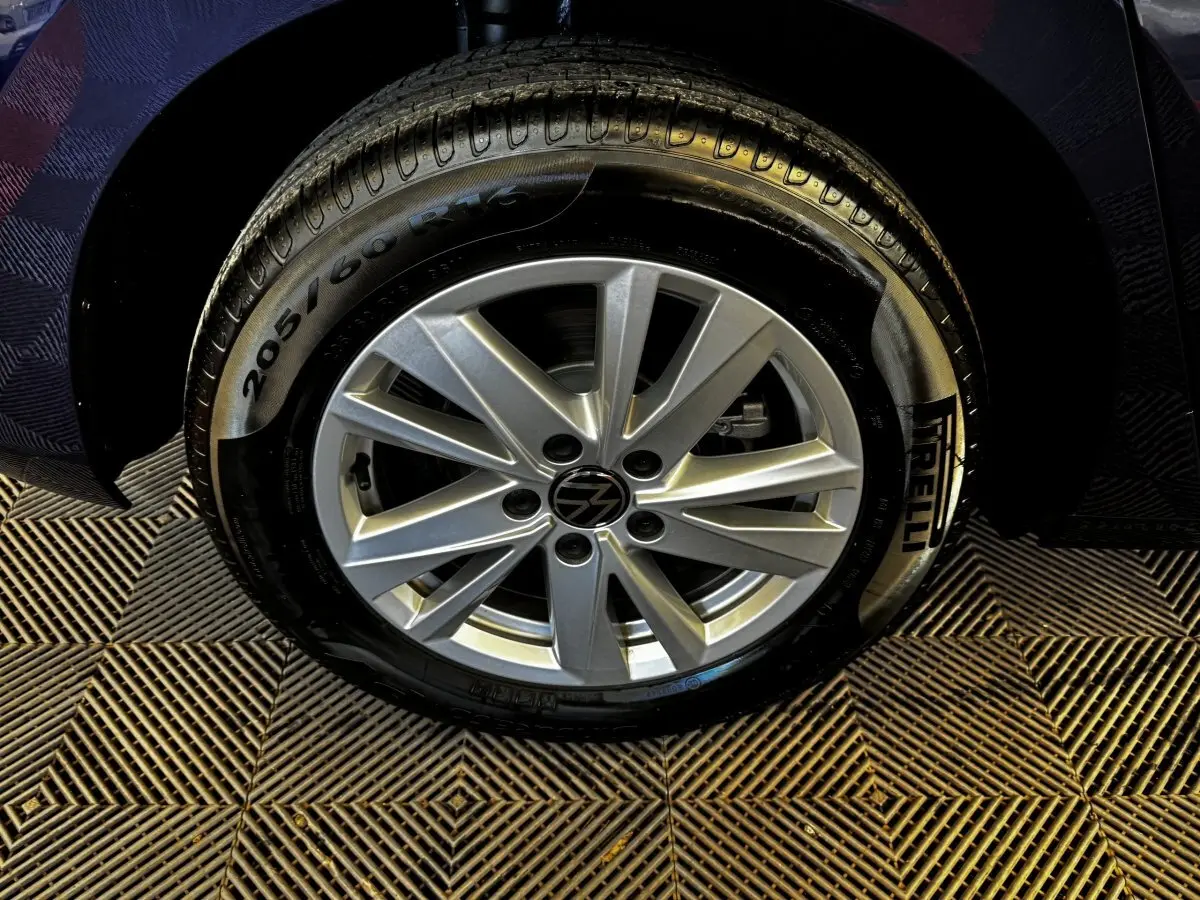 Gros plan sur la roue avant droite d’un Volkswagen Touran bleu 2024 avec jante alliage et pneu Pirelli.