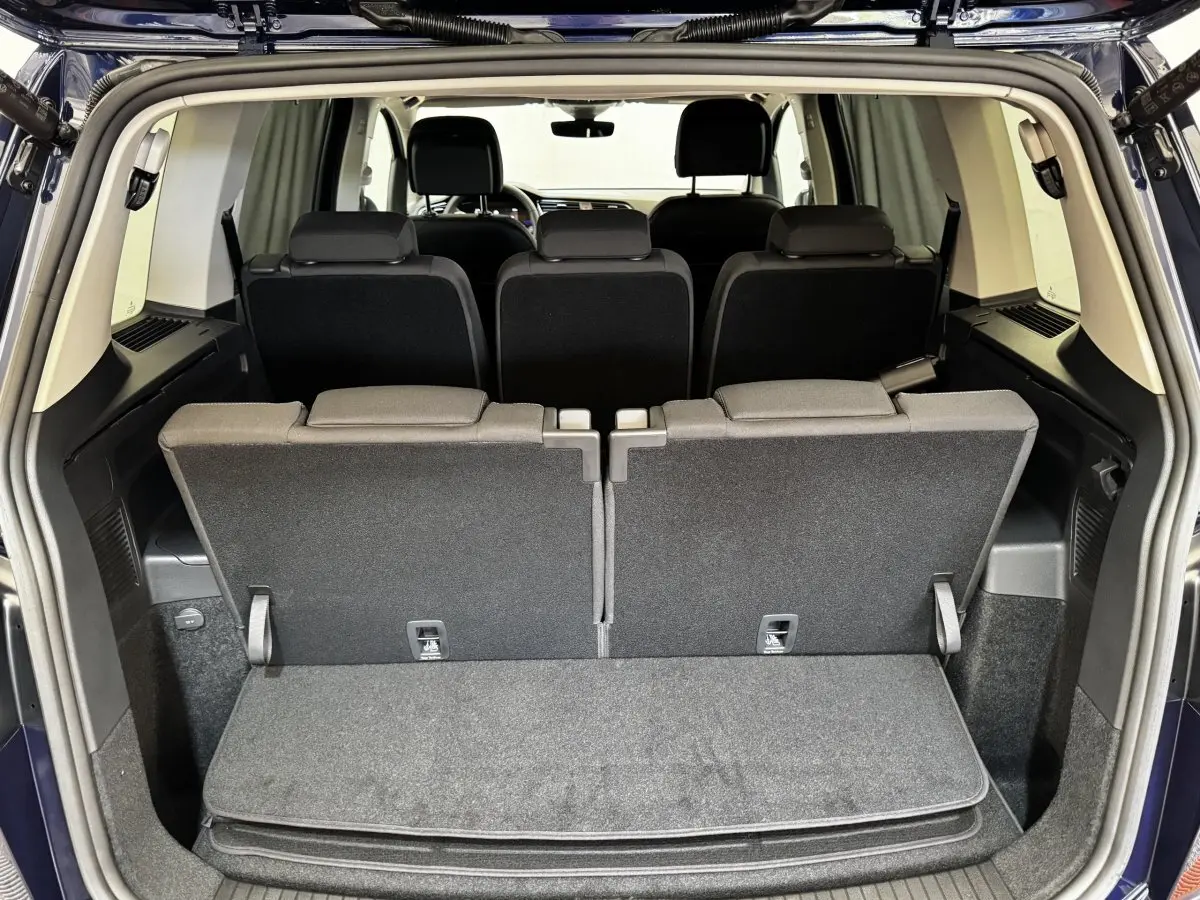 Vue arrière du coffre ouvert d’un Volkswagen Touran bleu 2024, montrant la troisième rangée de sièges relevée.