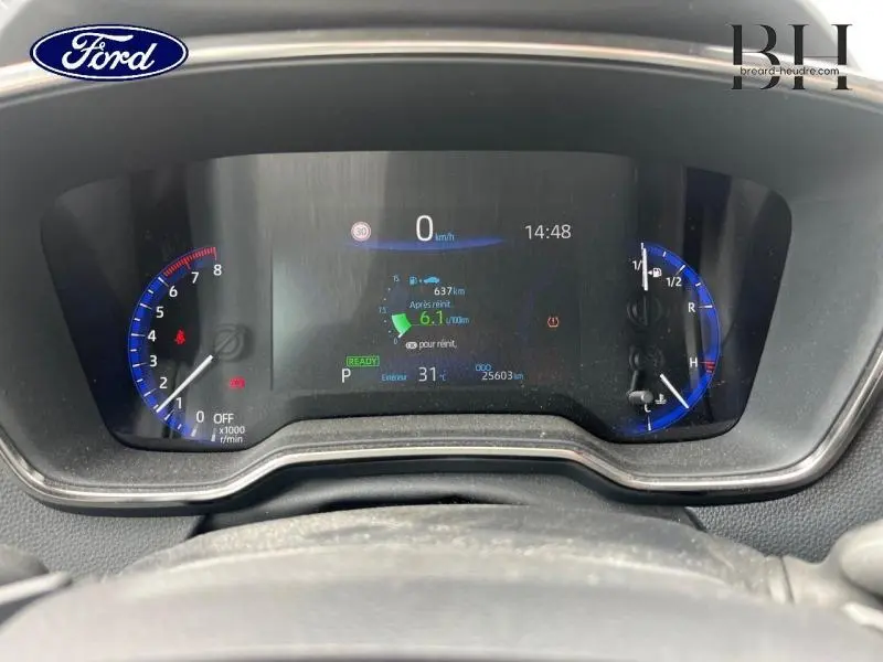 Tableau de bord numérique d'une Toyota Corolla blanche, affichant vitesse et informations moteur au centre.