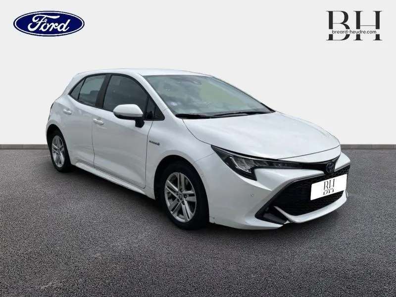 Toyota Corolla 184h Dynamic Business blanc pur vue 3/4 avant droit avec calandre noire et jantes alu.