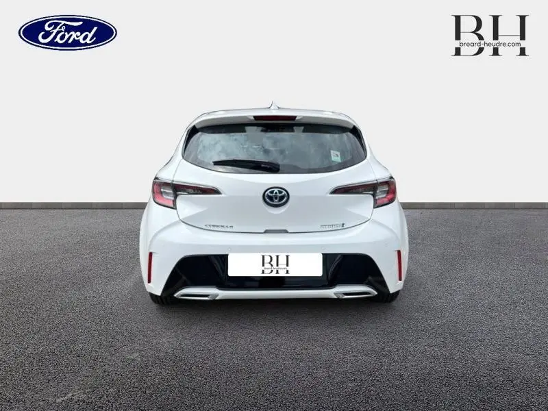 Vue arrière d'une Toyota Corolla 184h Dynamic Business blanche avec double sortie d'échappement chromée sur fond neutre.