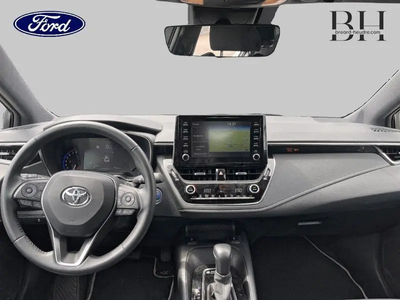 Tableau de bord et volant cuir d'une Toyota Corolla blanche, vue frontale mettant en valeur l'écran tactile central et les commandes au volant.