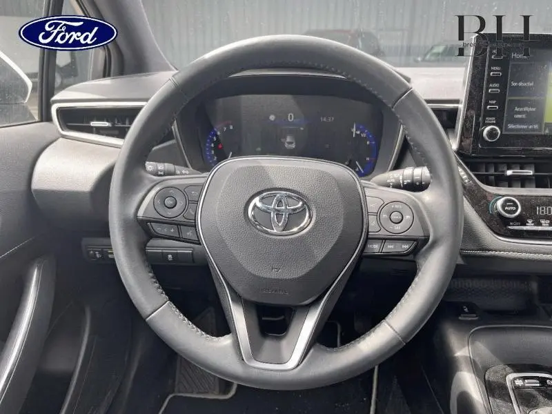 Vue rapprochée du volant cuir multifonction d'une Toyota Corolla blanche avec tableau de bord numérique et écran tactile.