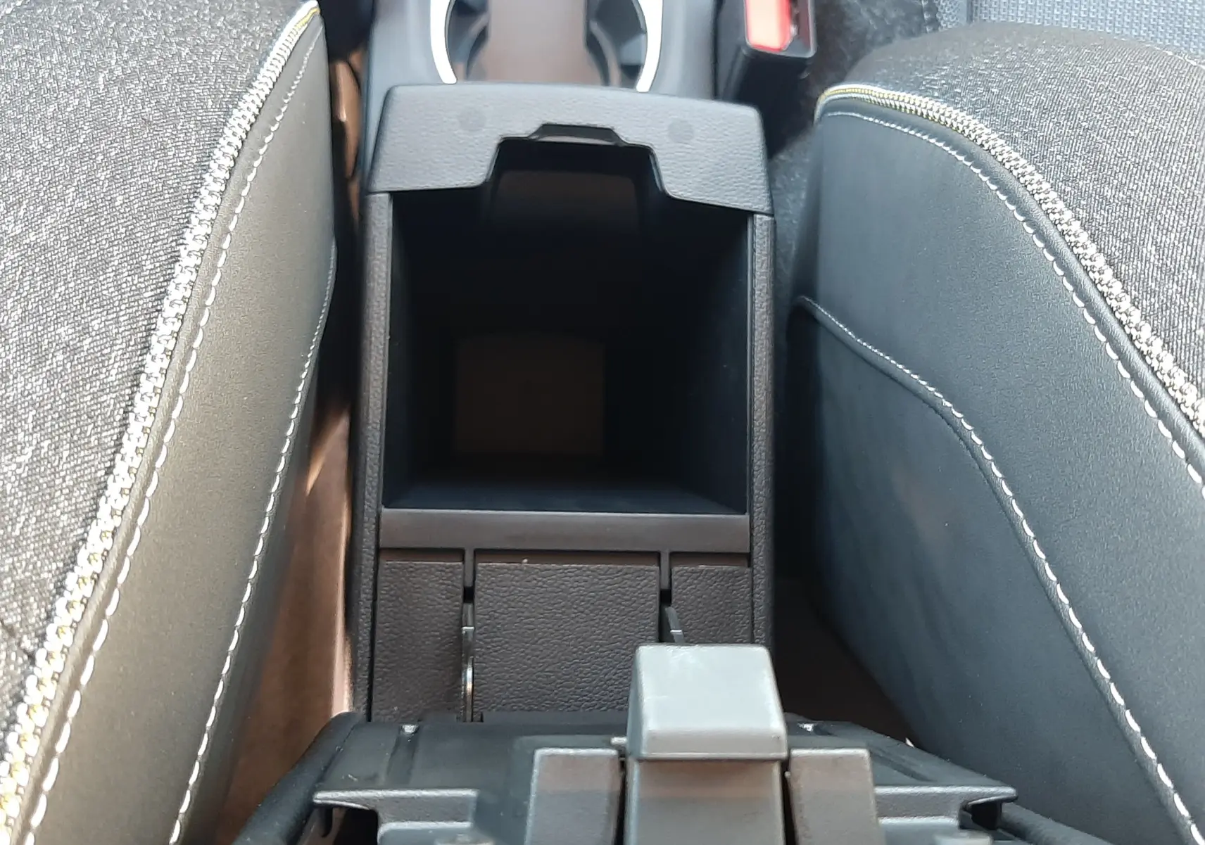 Vue rapprochée de la console centrale ouverte entre les sièges en tissu gris du Renault Captur bleu Iron 2025.