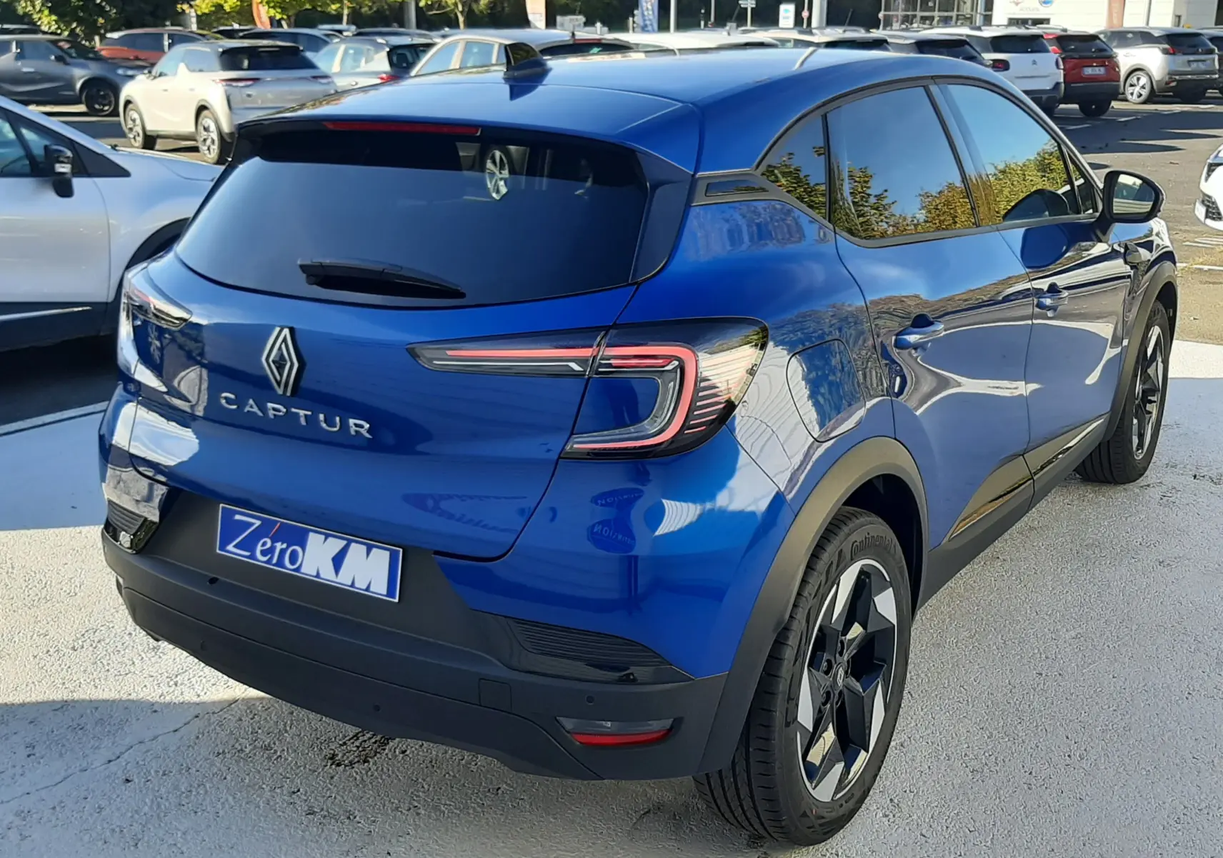 Vue 3/4 arrière droite d'un Renault Captur bleu Iron 2025 avec vitres teintées et jantes bi-ton noires.