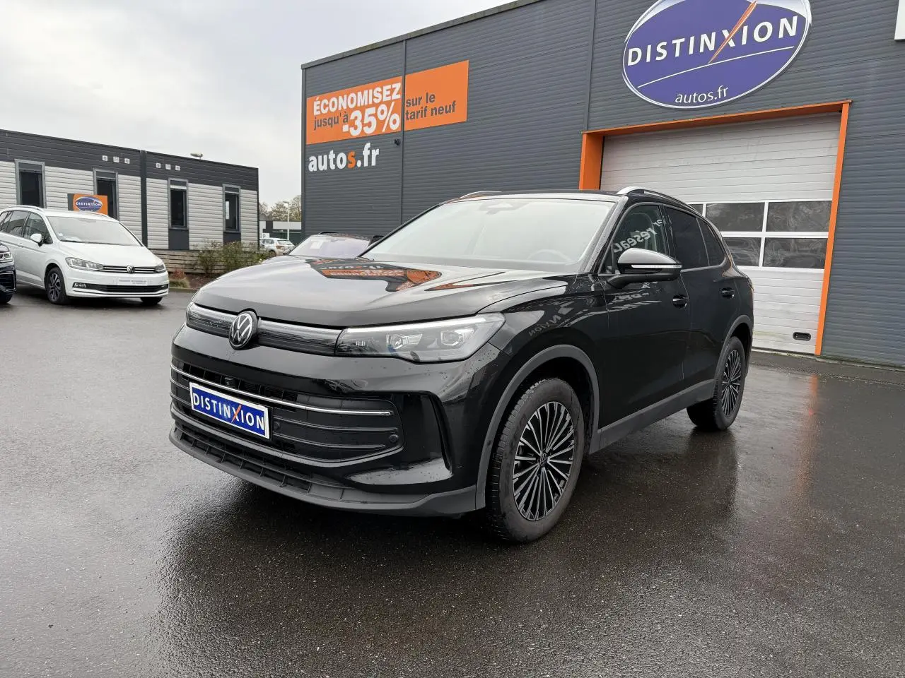 Volkswagen Tiguan noir grenadille métallisé vu en 3/4 avant droit sur parking devant un bâtiment commercial.