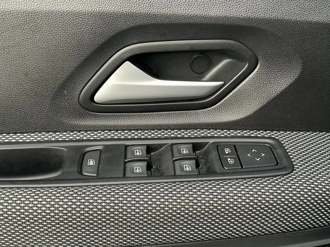 Gros plan sur la poignée intérieure et les commandes des vitres côté conducteur d'une Dacia Sandero blanche 2024.