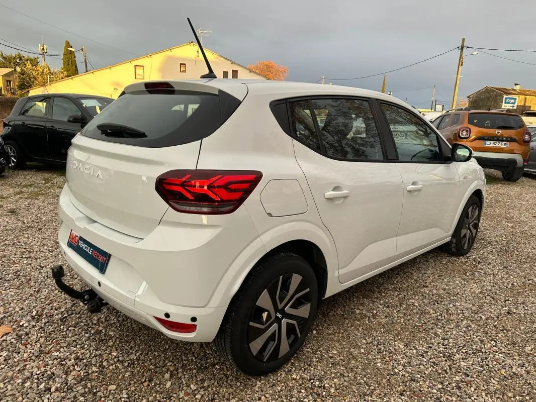 Vue 3/4 arrière droite d'une Dacia Sandero blanche 2024 avec feux arrière LED et attelage de remorque.