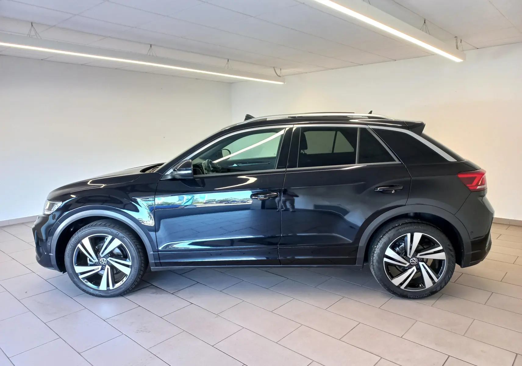 Vue de profil côté gauche d’un Volkswagen T-Roc 2025 noir intense avec jantes alliage et toit ouvrant panoramique.
