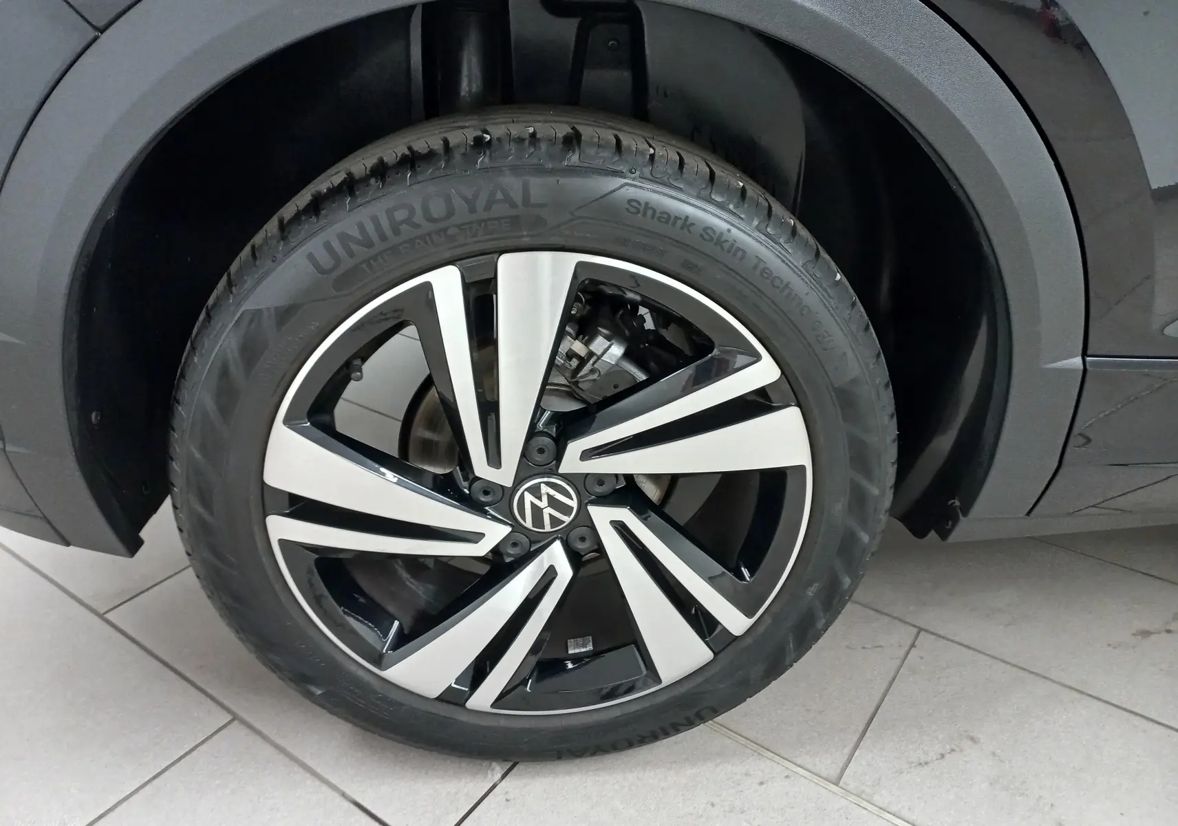 Gros plan sur la roue avant droite du Volkswagen T-Roc noir intense, mettant en valeur la jante alliage bicolore au design moderne.