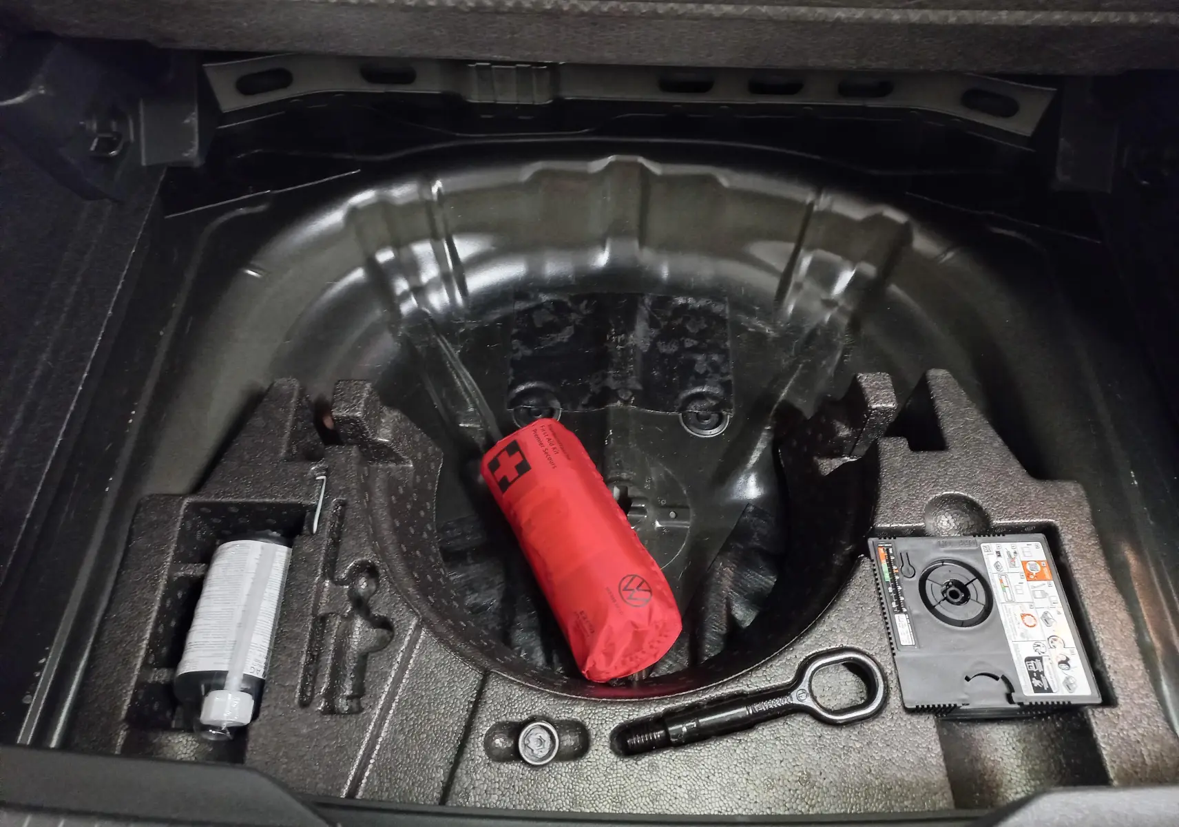 Vue plongeante sur le coffre ouvert du Volkswagen T-Roc 2025, montrant le rangement sous plancher avec kit de secours et compresseur.