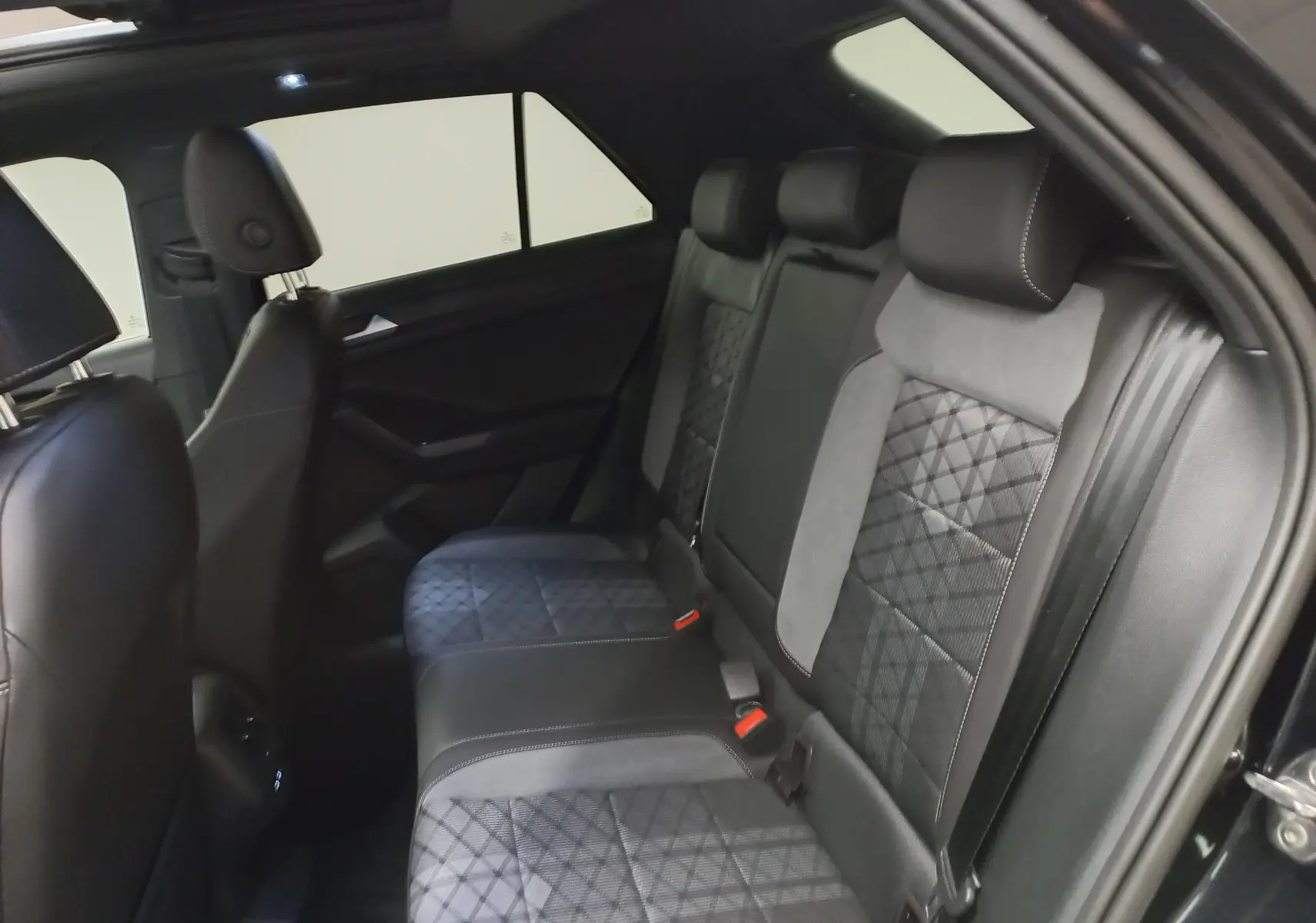 Vue intérieure côté droit des sièges arrière en cuir noir et tissu gris du Volkswagen T-Roc 2025 avec toit ouvrant panoramique.