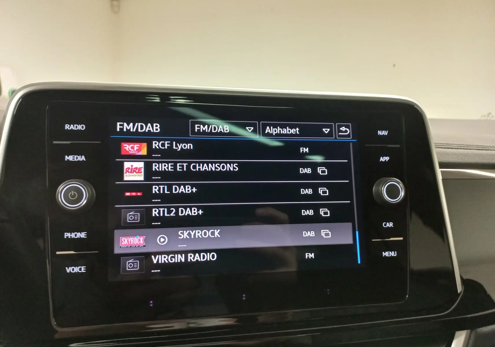Vue de face du tableau de bord du Volkswagen T-Roc 2025 noir intense, écran tactile affichant les radios FM/DAB.
