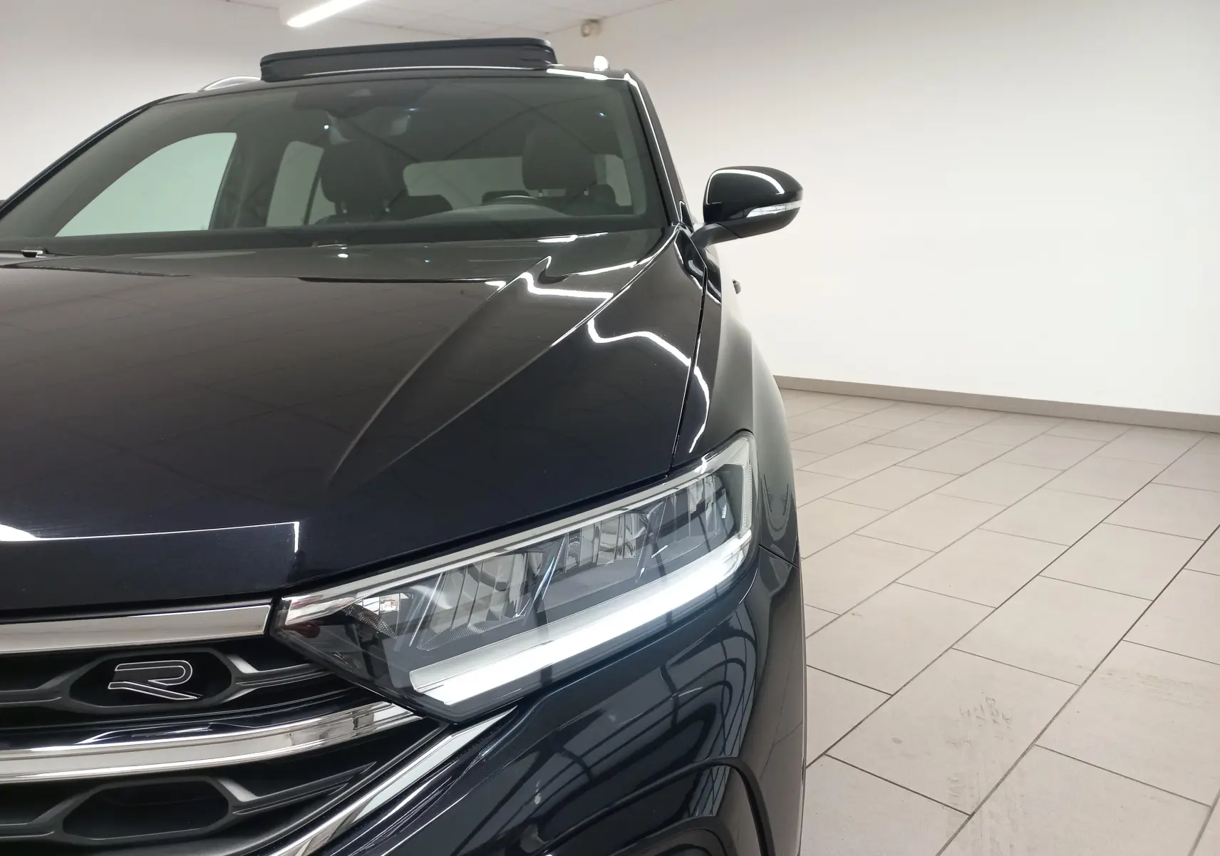 Vue avant droite du Volkswagen T-Roc noir intense avec projecteur LED allumé et toit ouvrant partiellement visible.