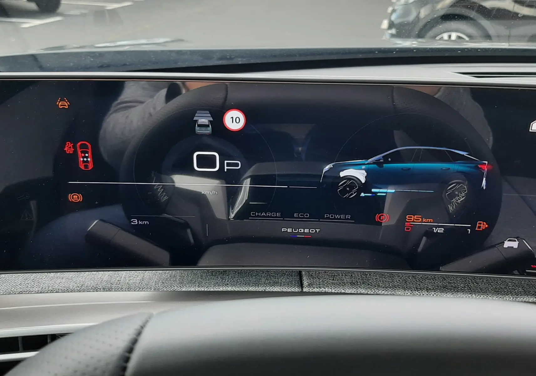 Vue du tableau de bord numérique du Peugeot 3008 hybride, affichant l'état de charge et la vitesse, avec reflet du volant.